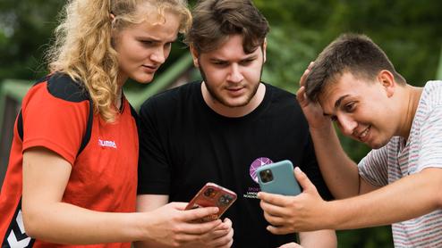 Drei Jugendliche stehen zusammen und schauen auf ihre Smartphones, um etwas anzusehen oder zu besprechen.