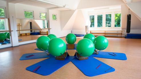 Fitnessraum mit grünen Gymnastikbällen auf blauen Matten, umgeben von Spiegeln und Fenstern.