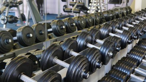 Reihe von schwarzen Hanteln auf einem Ständer in einem Fitnessstudio, mit Spiegel im Hintergrund.