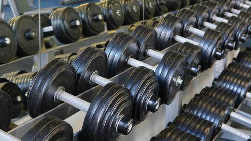 Reihe von schwarzen Hanteln auf einem Ständer in einem Fitnessstudio, mit Spiegel im Hintergrund.