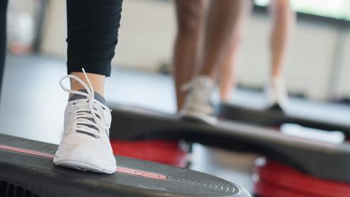 Nahaufnahme eines Fußs mit einem weißen Sport-Schuh auf einer Fitness-Stepp-Platte während eines Workout.