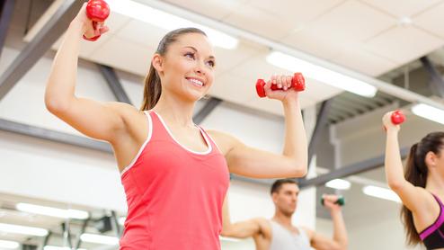 Vier Personen heben Gewichte in einem Fitnessstudio. Zwei Frauen tragen Sporttops, ein Mann hat ein T-Shirt an.