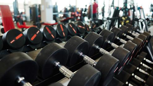 Reihe von schwarzen Hanteln auf einem Gestell in einem modernen Fitnessstudio mit unscharfem Hintergrund.