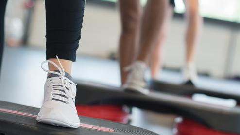 Nahaufnahme eines Fußs mit einem weißen Sport-Schuh auf einer Fitness-Stepp-Platte während eines Workout.