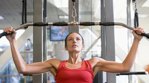 Frau in rotem Top trainiert an einer Kraftmaschine mit Latzuggriff im Fitnessstudio.