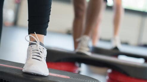 Nahaufnahme eines Fußs mit einem weißen Sport-Schuh auf einer Fitness-Stepp-Platte während eines Workout.