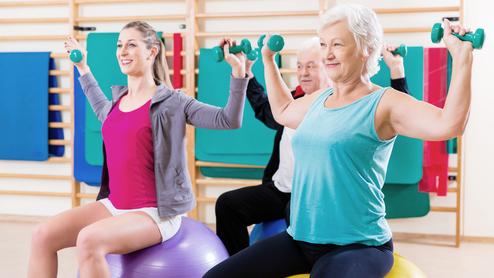 Drei Personen mit Hanteln sitzen auf großen Gymnastikbällen und trainieren in einem Fitnessraum.