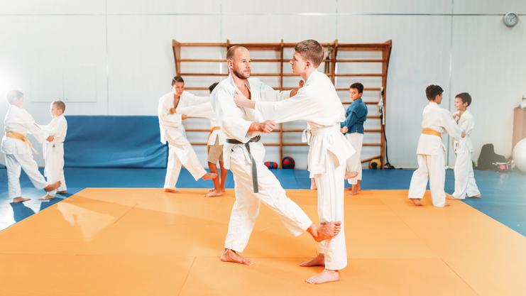Junge Judoka in weißen Anzügen üben Techniken auf einer orangefarbenen Judomatte in einem Sportverein.