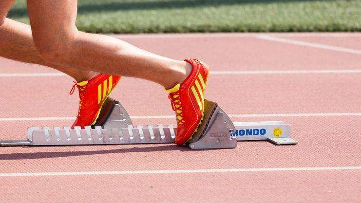 Nahaufnahme eines Fußes in einem roten Laufschuh, der auf einem Startblock auf einer Laufbahn steht.
