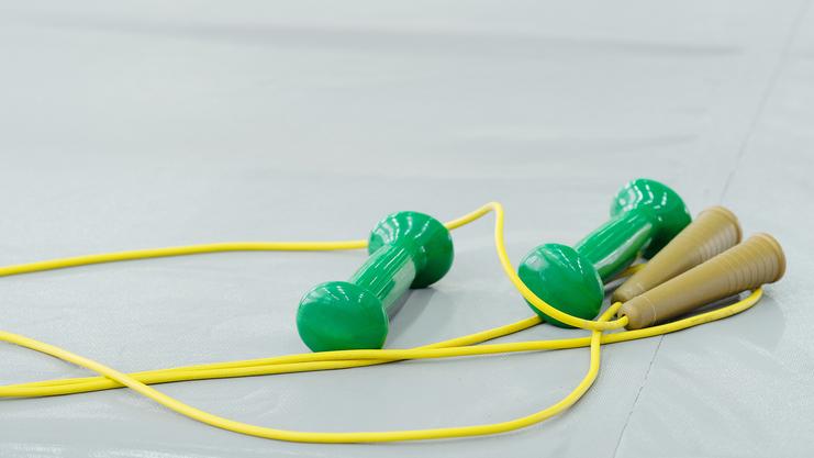 Grüne Dumbbells und ein Seil aus gelben Drähten liegen auf einer hellgrauen Trainingsmatte.