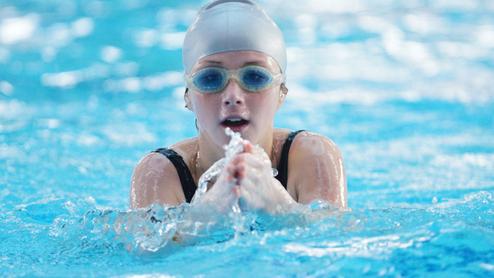 Junge Schwimmerin mit Badekappe und Schwimmbrille, die durch das Wasser paddelt. Blasen spritzen um sie herum.
