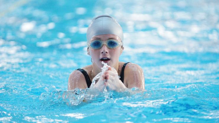 Junge Schwimmerin mit Badekappe und Schwimmbrille, die durch das Wasser paddelt. Blasen spritzen um sie herum.
