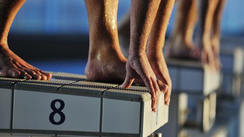 Nahaufnahme von Füßen und Händen von Schwimmern, die auf einem Startblock mit der Nummer 8 stehen.