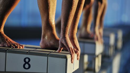 Nahaufnahme von Füßen und Händen von Schwimmern, die auf einem Startblock mit der Nummer 8 stehen.