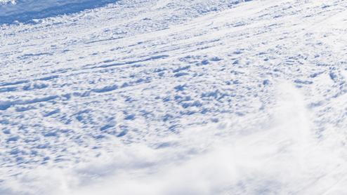 Kind fährt in Ski-Ausrüstung auf einer verschneiten Piste mit Bergen im Hintergrund und klarem blauen Himmel.