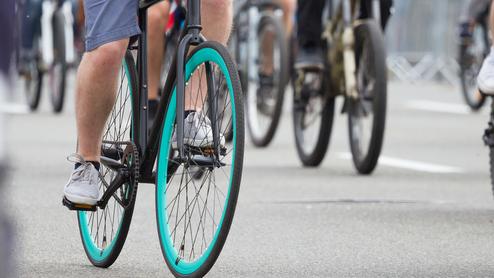 Nahaufnahme eines Fahrradfahrers mit blaugrünen Reifen, umgeben von weiteren Radfahrern auf einer Straße.