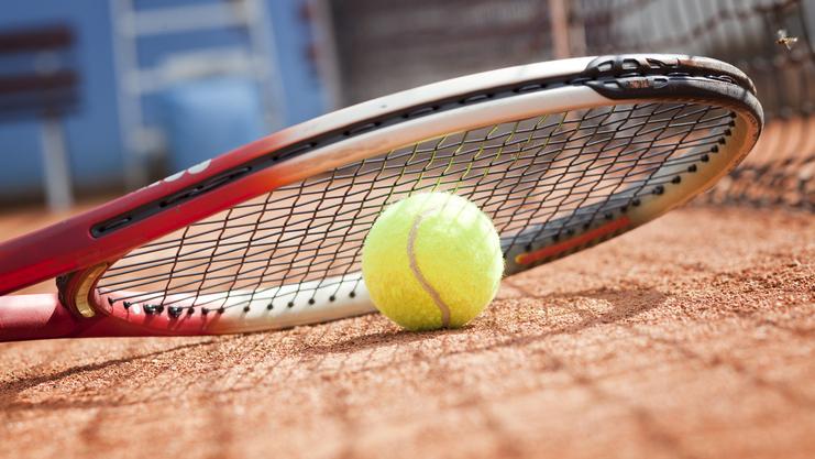 Tennisball liegt auf einem Platz neben einem Tennisracket auf dem Sandboden.