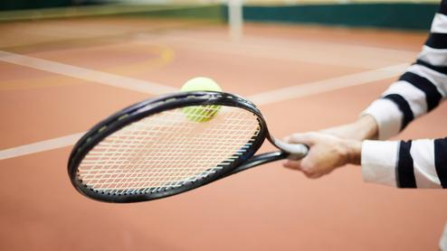 Nahaufnahme einer Hand, die einen Tennisschläger hält, während ein Tennisball in Richtung Schläger fliegt.