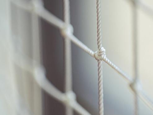 Nahaufnahme eines weißen Netzgewebes mit Knoten, unscharf im Hintergrund.